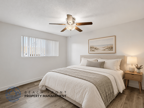 A bedroom with a bed, a ceiling fan, and a nightstand with a lamp.