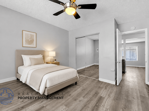 A bedroom with a bed, a ceiling fan, and a wooden floor.