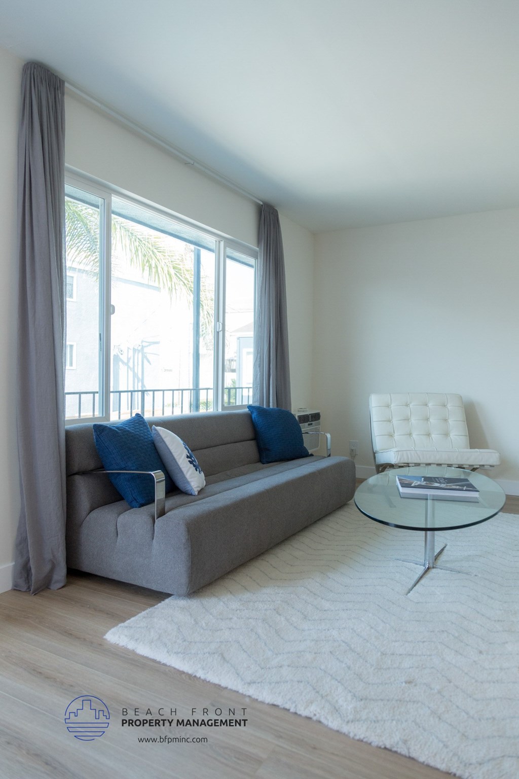 A living room with a grey couch, a white chair, and a glass table.