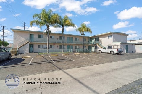 A parking lot with a building and palm trees in the background.