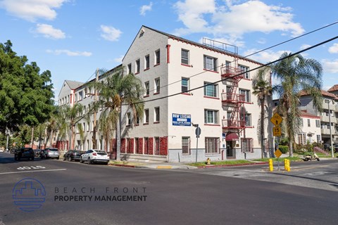 a large white building at the corner of a street with palm trees