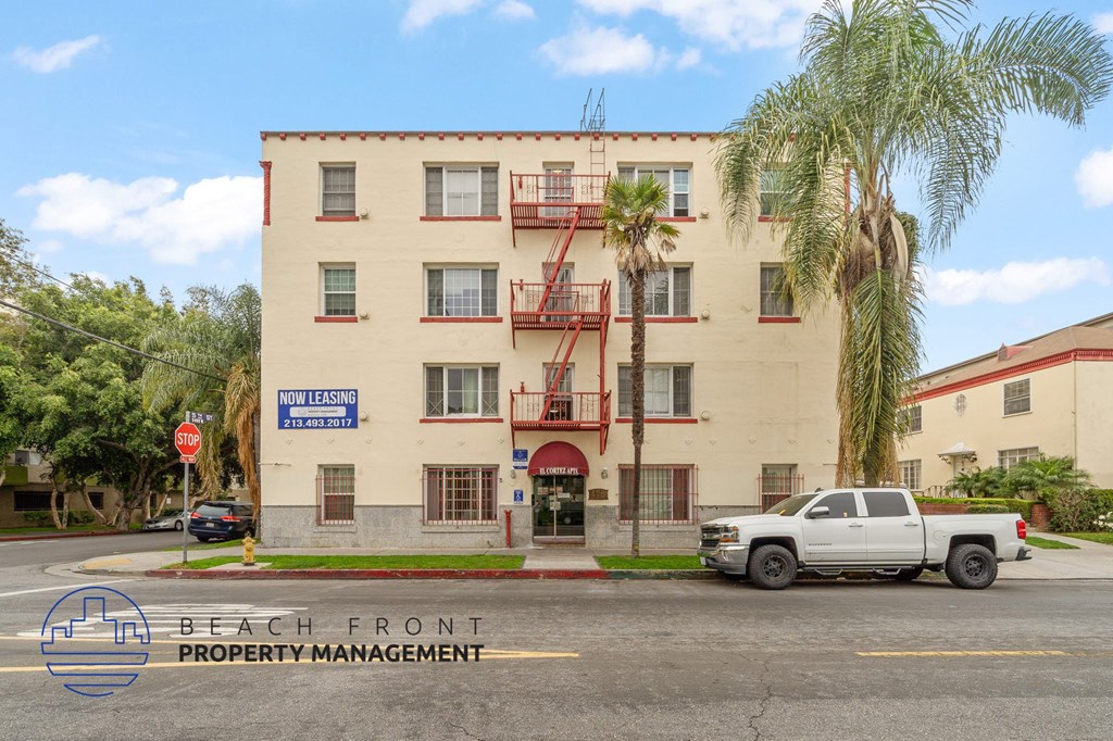 A white building with a sign that says "Now Leasing" in front of it.