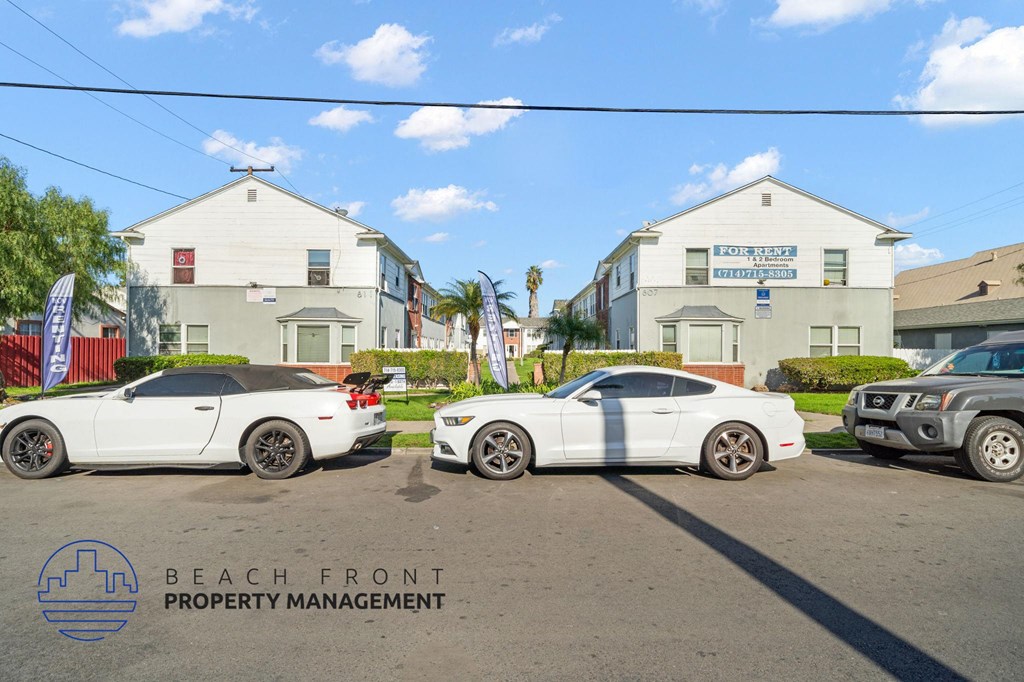 Three white cars are parked in front of a building with a sign that reads "Beach Front Property Management.".