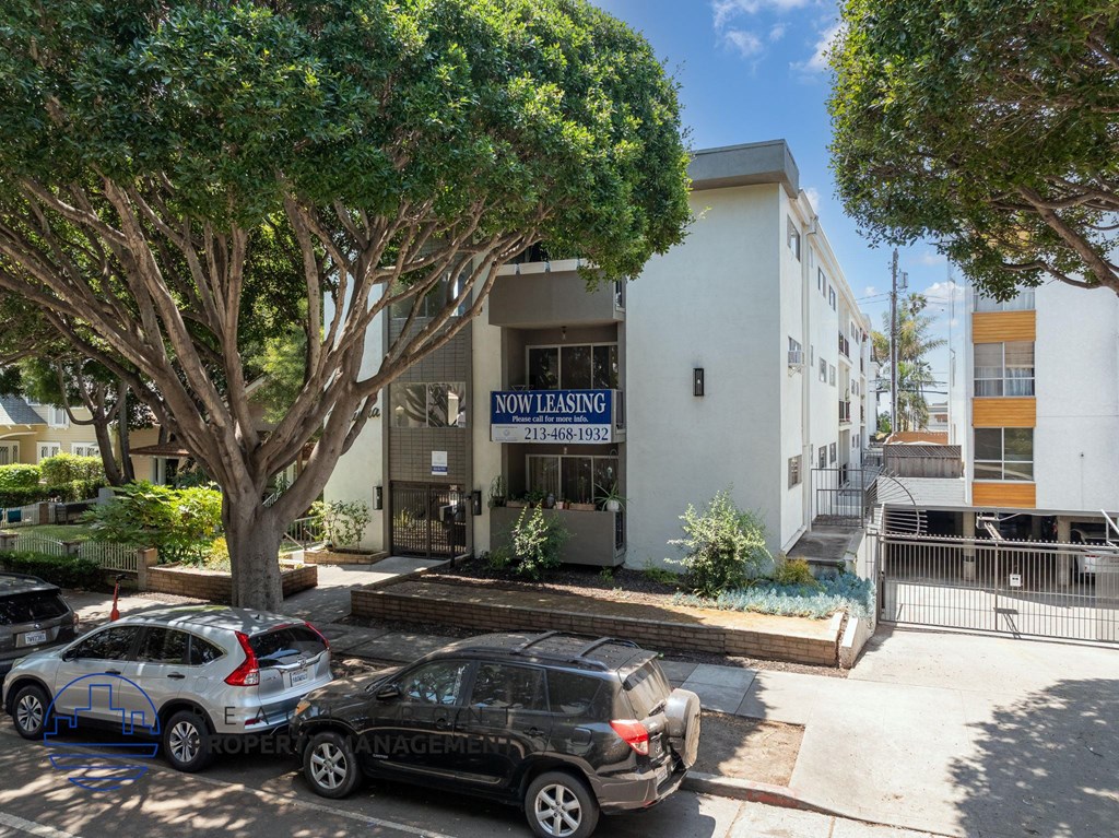 A parking lot with cars and a building that says "NOW LEASING" in front of it.