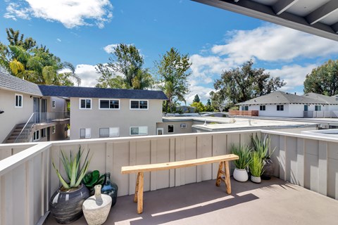 A wooden bench sits on a patio with a potted plant and vase beside it.