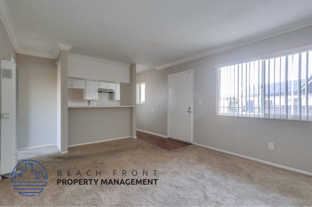 an empty living room with a kitchen and a large window