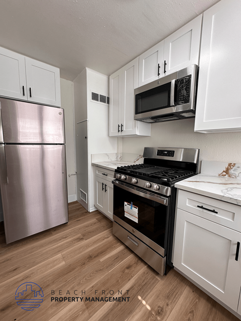 A kitchen with a stainless steel refrigerator, a stove, and white cabinets.