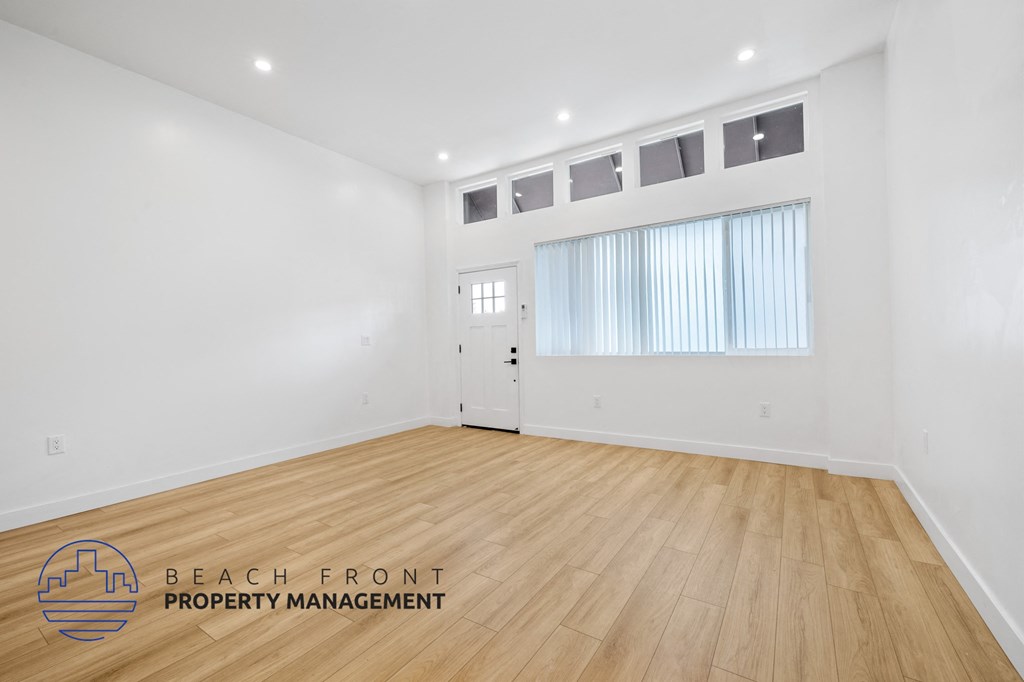 a living room with white walls and wood flooring and a white door