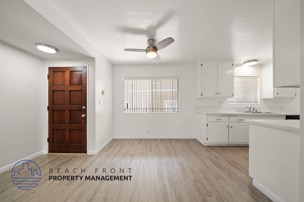 A spacious kitchen and living room with a wooden door and a ceiling fan.