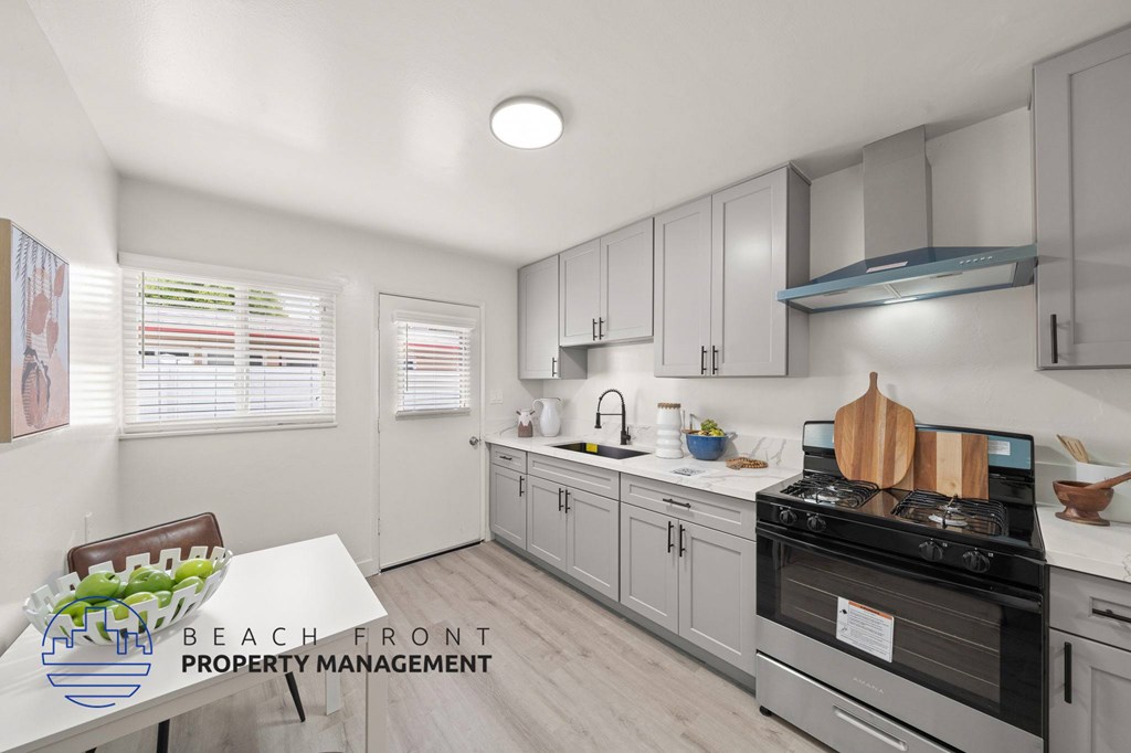 A kitchen with a stove top oven and a dining table with a bowl of fruit on it.
