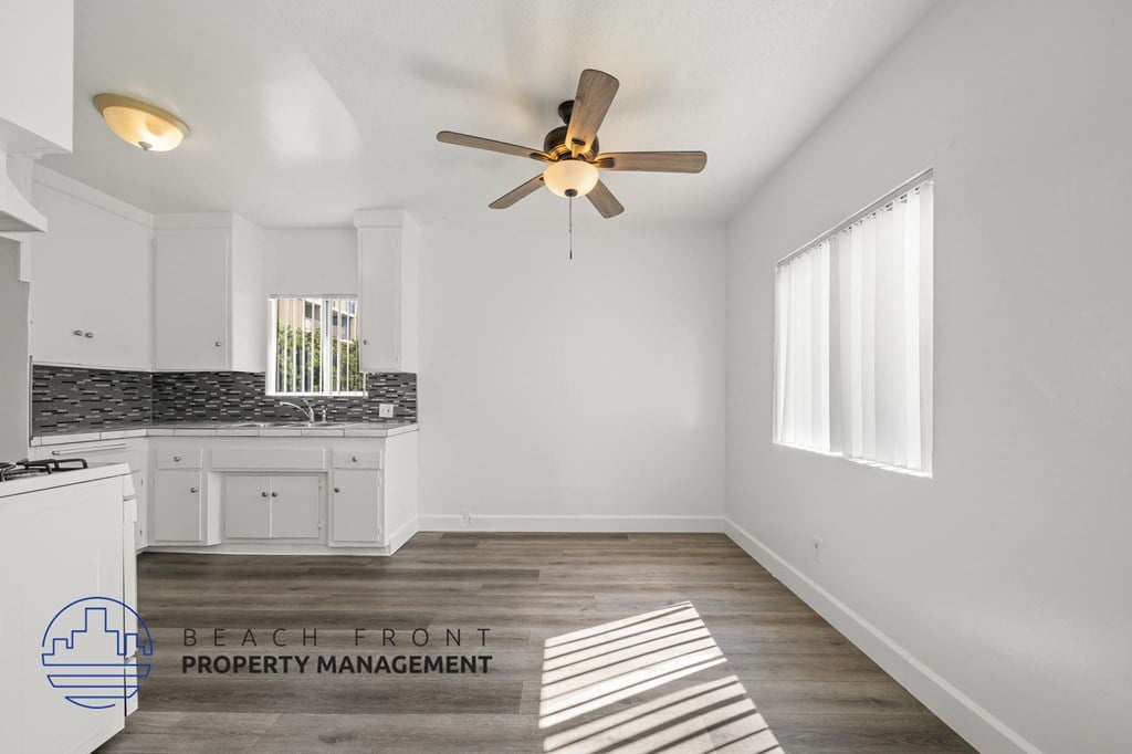 A well-lit, spacious kitchen and living room with a ceiling fan and wooden flooring.