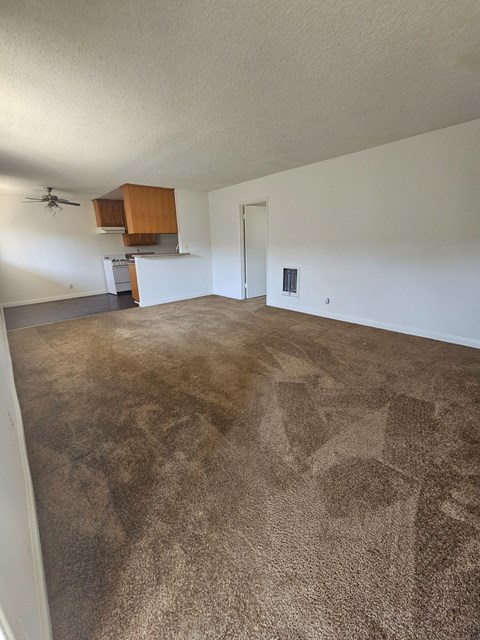 an empty living room with carpet and a kitchen