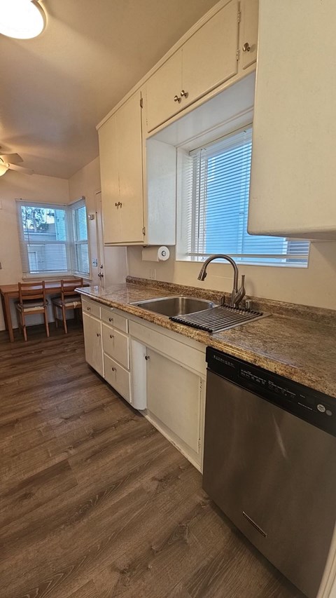 A kitchen with a stainless steel dishwasher and wooden floors.