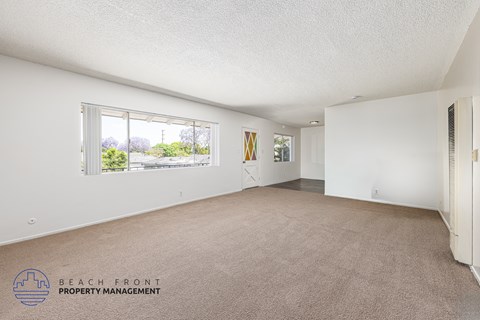 A spacious room with a carpeted floor and a window overlooking a beach.