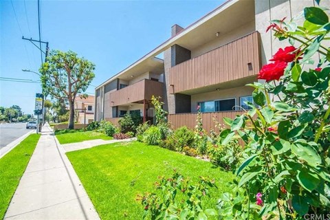 a sidewalk in front of an apartment building with green grass and flowers