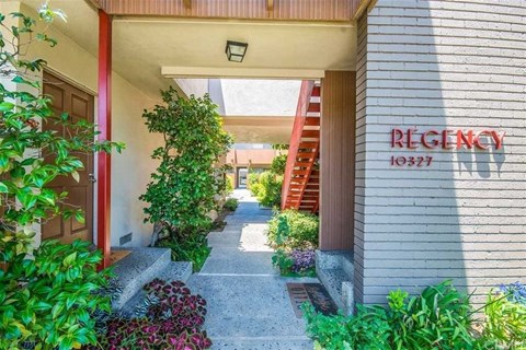 the entrance to a condo building with a walkway and plants