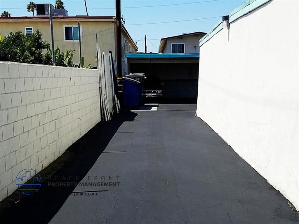 a driveway with a white brick wall and a blue trash can