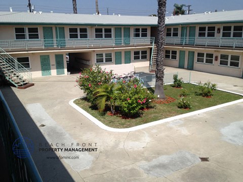A courtyard with a palm tree and flowers in front of a building with balconies.