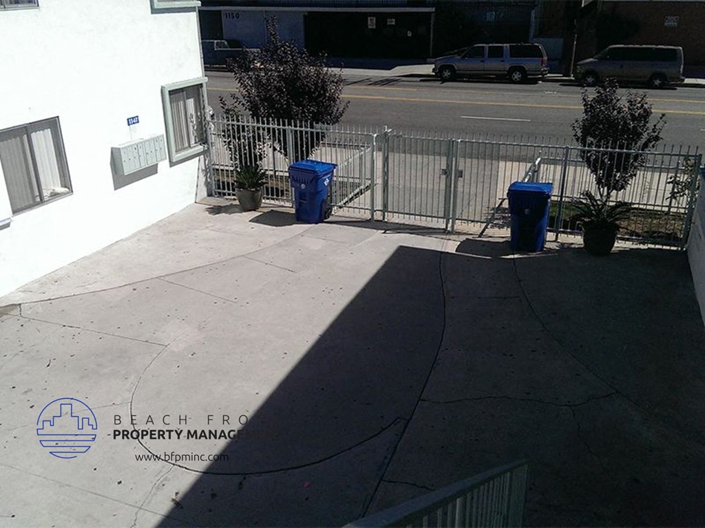 three blue trash cans on a sidewalk next to a fence
