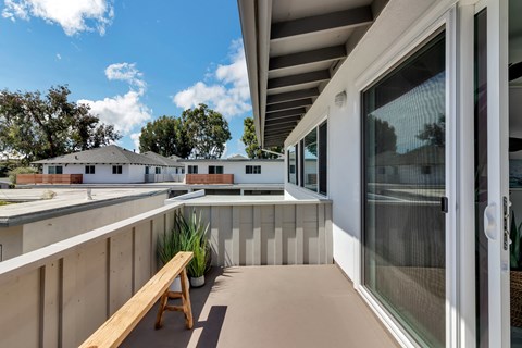 A wooden bench is on a patio with a glass door.