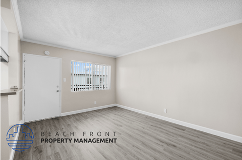 the spacious living room of an apartment with wood flooring and a door to the