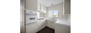 an empty kitchen with white cabinets and appliances and a window