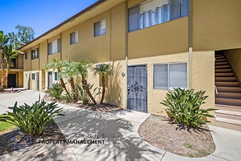 a yellow building with a blue door and plants in front of it