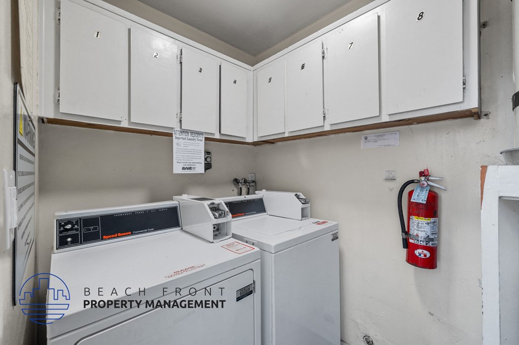 A white washing machine is in a small laundry room with a fire extinguisher on the wall.