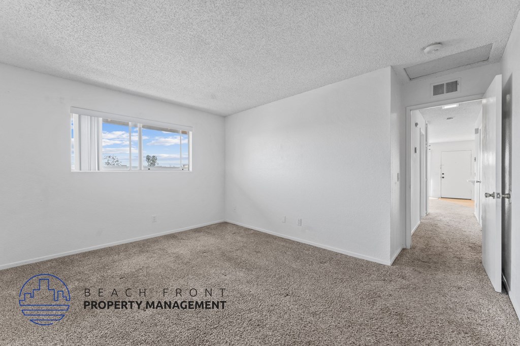 A spacious room with a carpeted floor and a window showing a beach view.