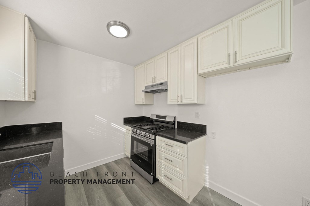 A kitchen with white cabinets and black countertops.