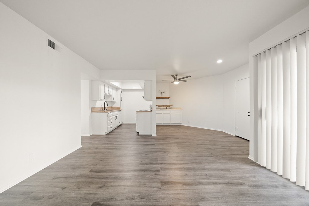 a living room and kitchen with white walls and wood floors