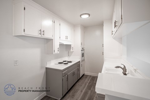 A clean, white kitchen with wooden floors and a logo for Beach Front Property Management.