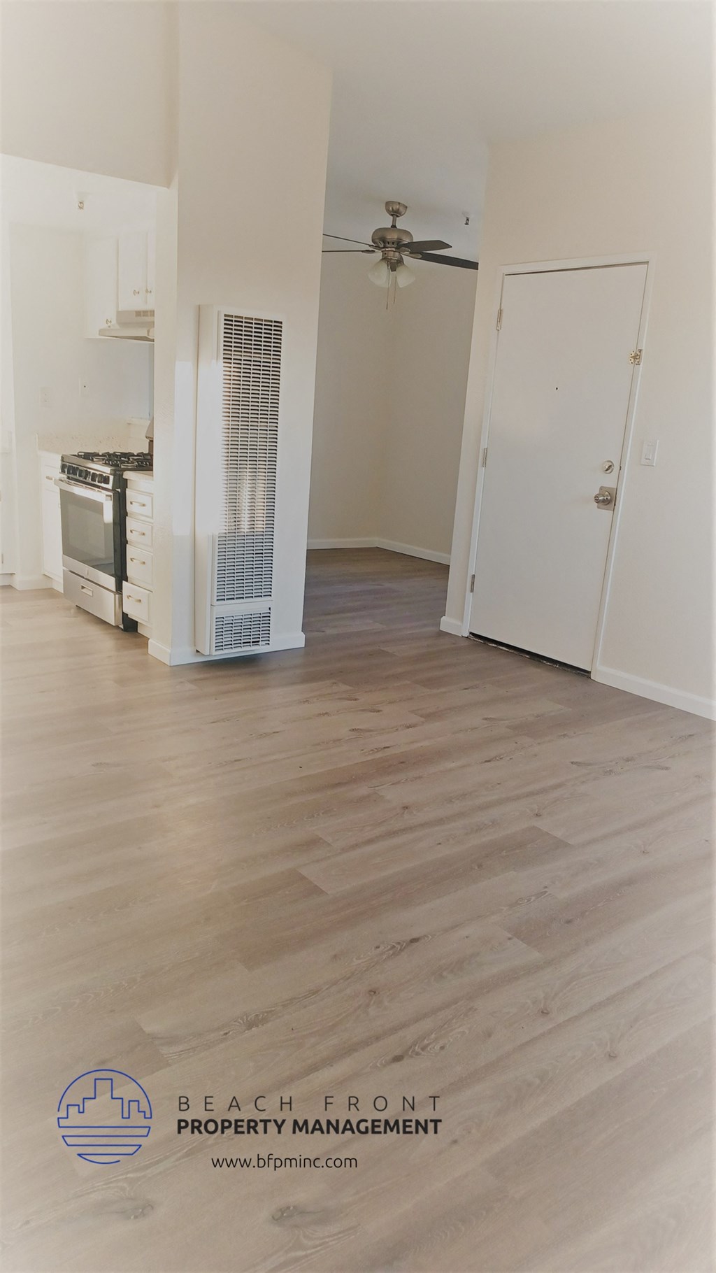an empty living room with wood flooring and a kitchen