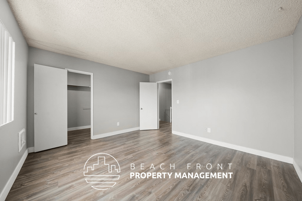 the spacious living room of an apartment with wood flooring and white walls