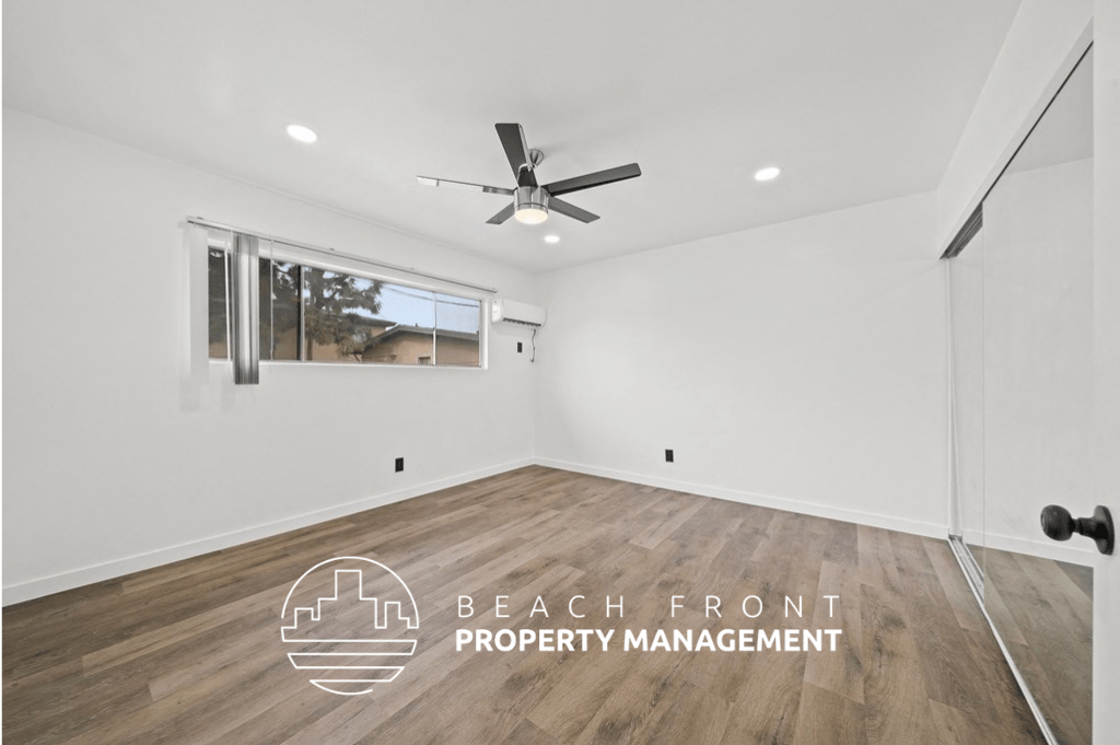 a living room with white walls and wood flooring and a ceiling fan