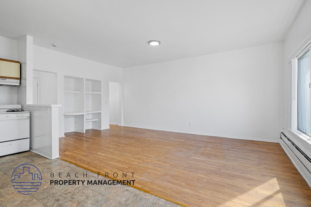 A spacious room with wooden floors and white walls, with a logo for Beach Front Property Management in the bottom left corner.