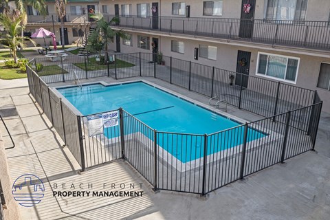 A pool surrounded by a black fence with the words Beach Front Property Management on it.