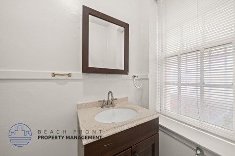 A bathroom with a sink, mirror, and window with blinds.