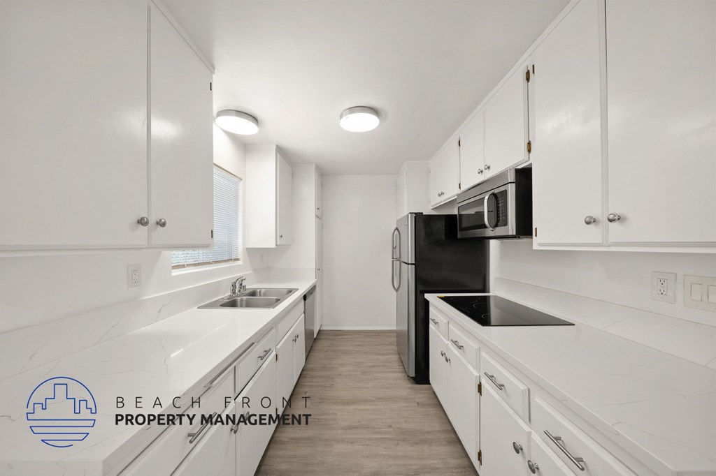 A kitchen with white cabinets and appliances, with a logo for Beach Front Property Management in the bottom left corner.