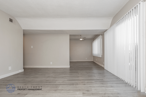 A spacious room with wooden flooring and white curtains on the window.