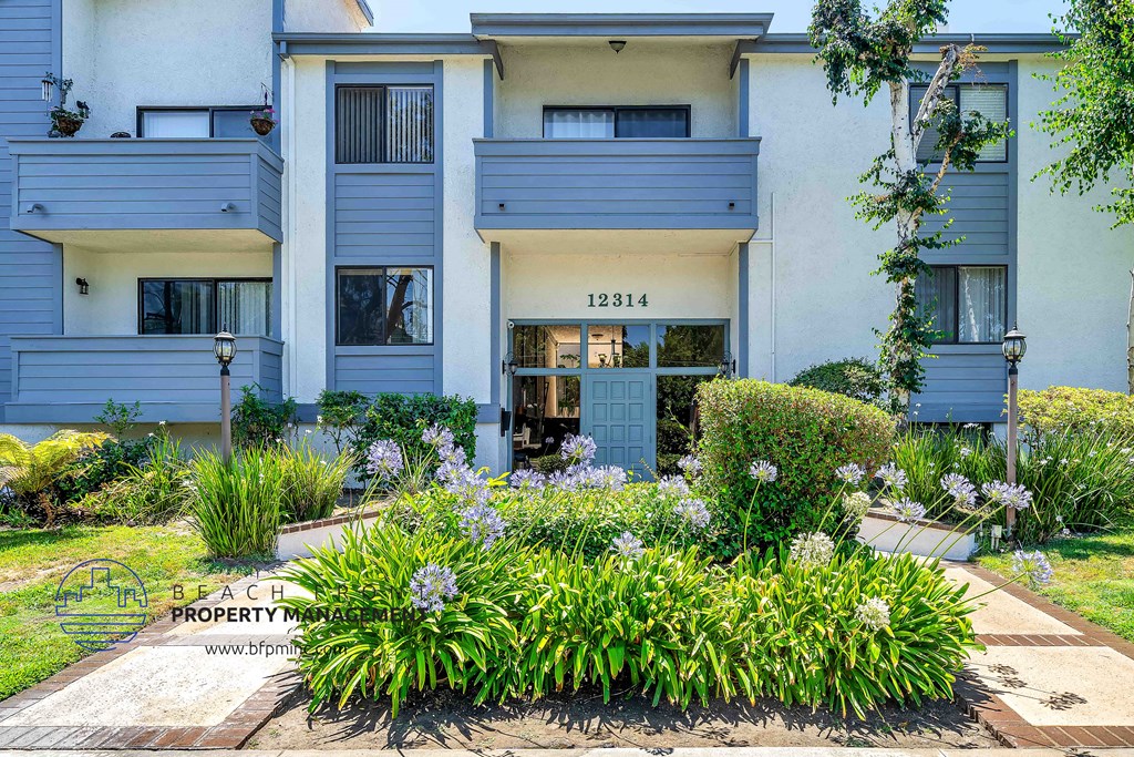 an apartment building with blue and white siding and a flower garden in front of it