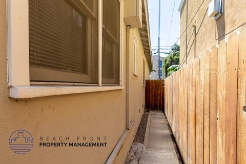 the side of a building with a sidewalk and a wooden fence