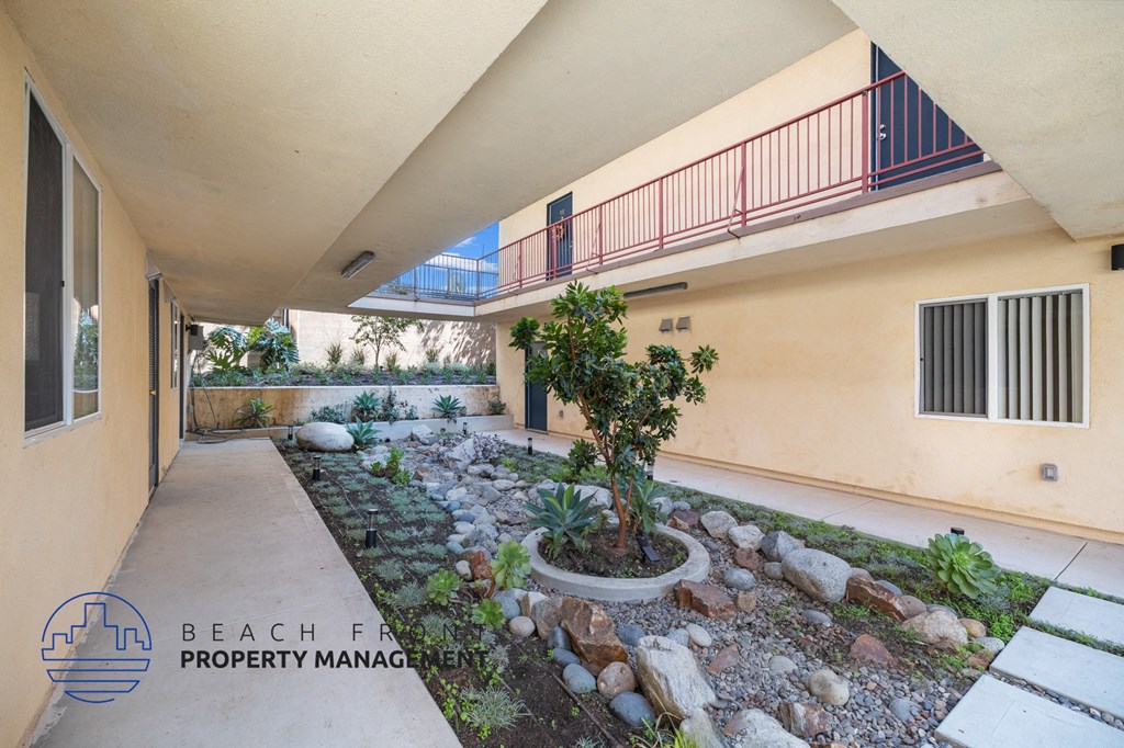 A balcony with a red railing overlooks a landscaped garden area.