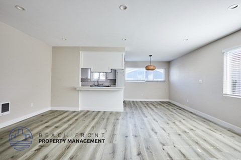 A spacious room with wooden flooring and a logo for Beach Front Property Management in the corner.