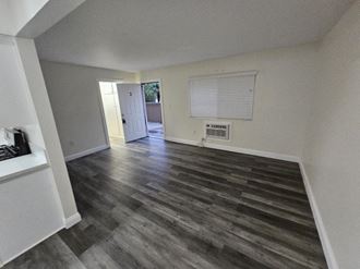 an empty living room with hardwood floors and a door to the kitchen