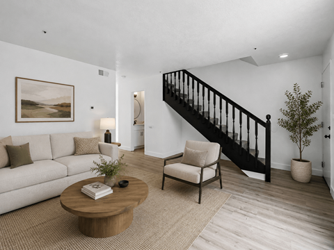 A living room with a white couch, a wooden coffee table, a chair, a potted plant, and a painting on the wall.
