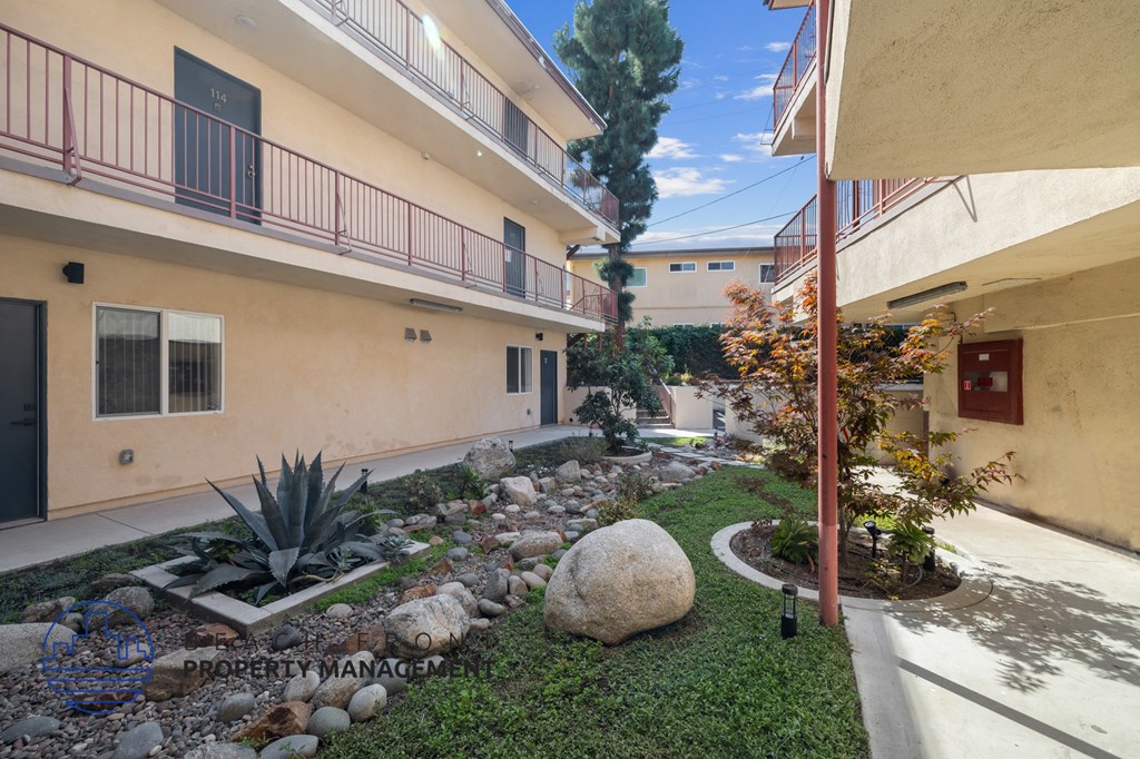 A courtyard with a rock in the middle and a tree on the right.