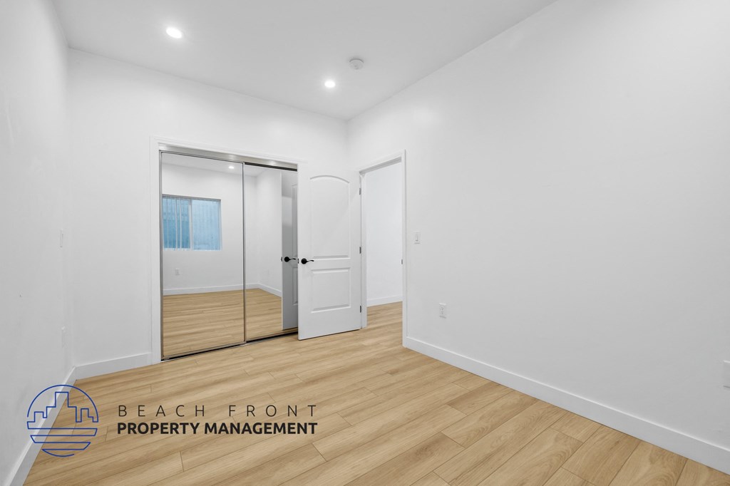 a renovated living room with white walls and wood flooring and a mirrored closet