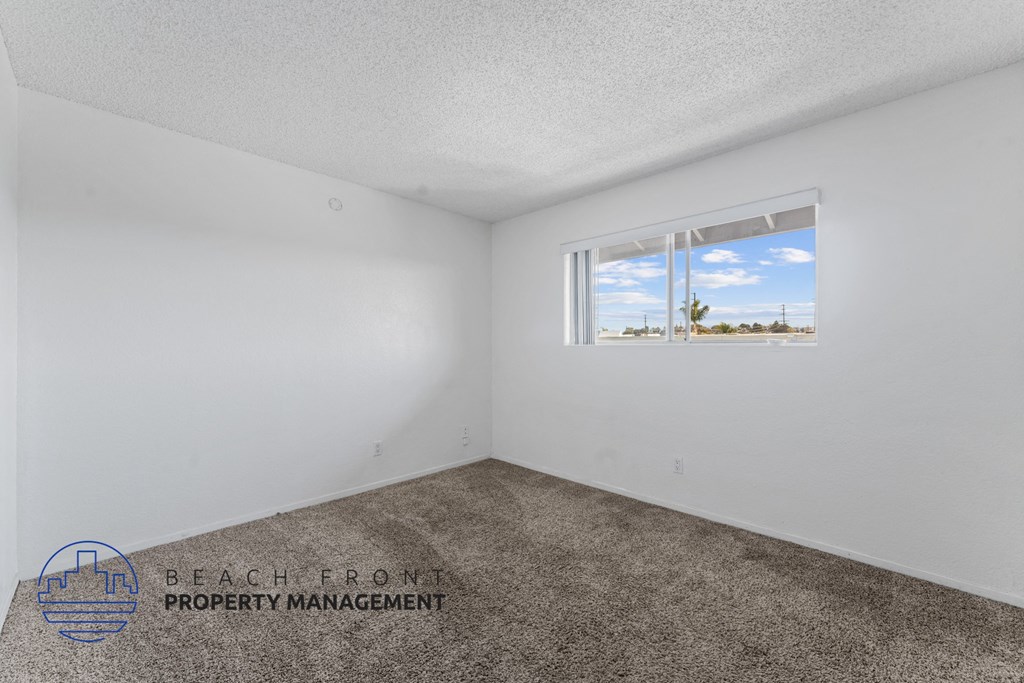 A room with a carpeted floor and a window showing a blue sky with clouds.
