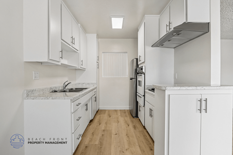 A kitchen with white cabinets and appliances, and a logo for Beach Front Property Management in the bottom left corner.